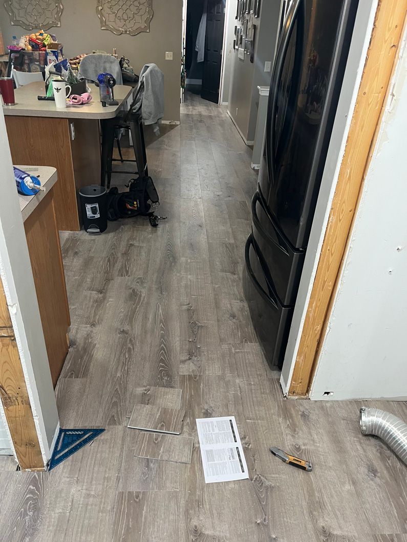 Hallway with light wood-look flooring, refrigerator, open doorway to kitchen with table, supplies, and papers.