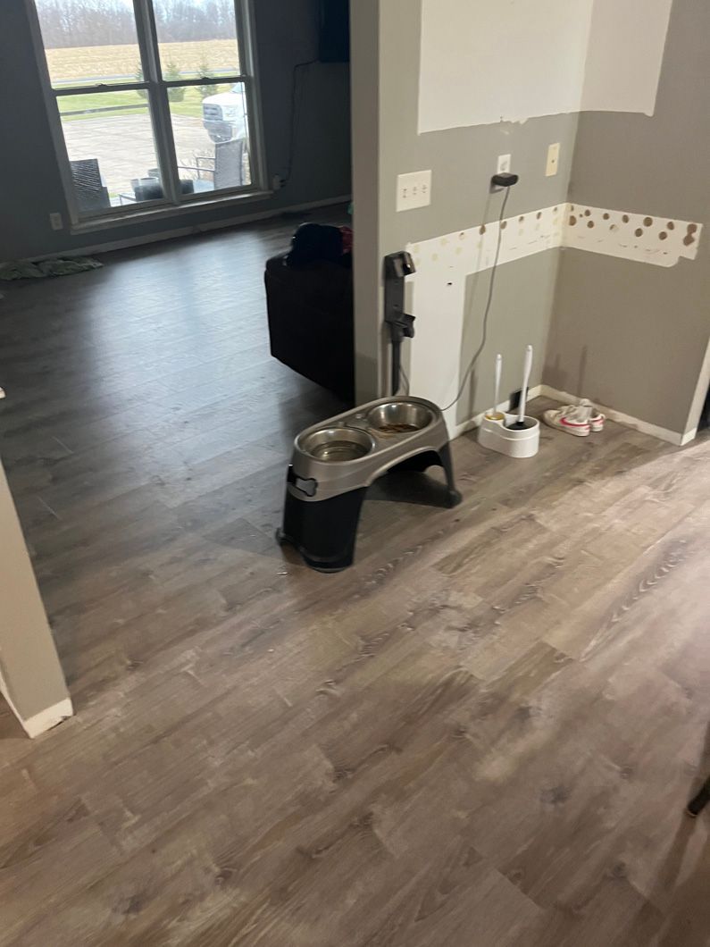 Gray wood-look flooring in a home. A dog bowl stand is visible. Walls are partially finished.