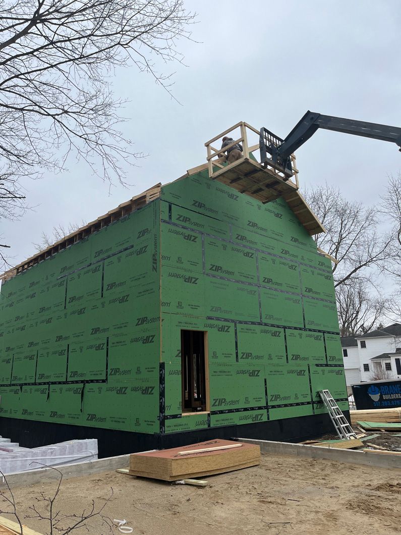 Construction site: Green-wrapped building with workers on lift, setting roof materials.