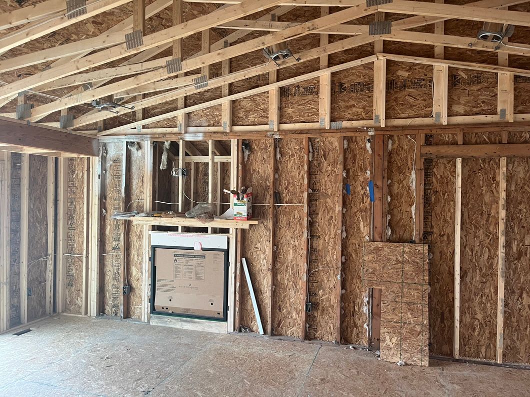 Interior of a building under construction. Walls and roof frame are wood; sunlight streams through.