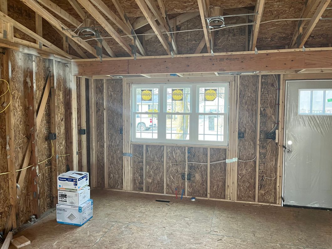 Interior of a building under construction, showing wooden framing, window, door, and boxes.