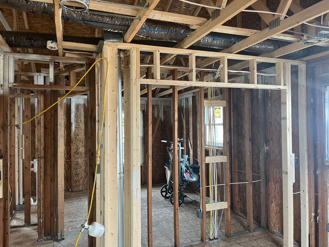 Interior framing of a room under construction, showing walls, ceiling beams, and electrical wiring.