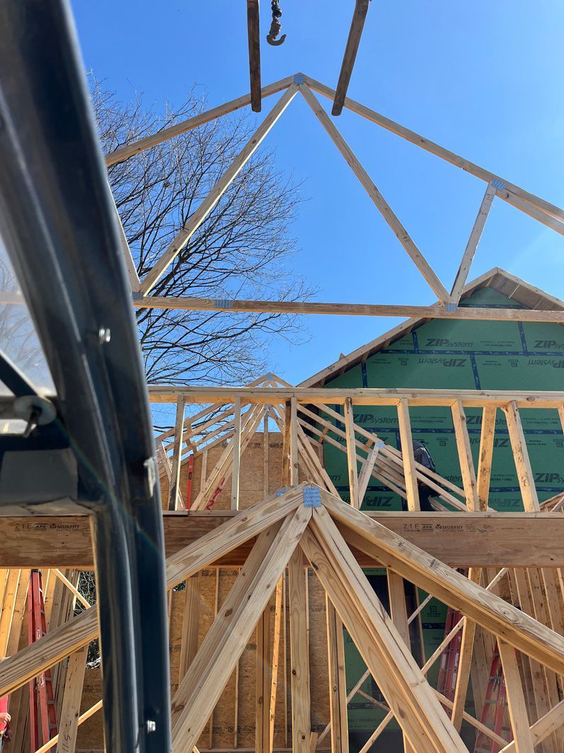 Wooden roof trusses being constructed on a building, viewed from below against a blue sky.
