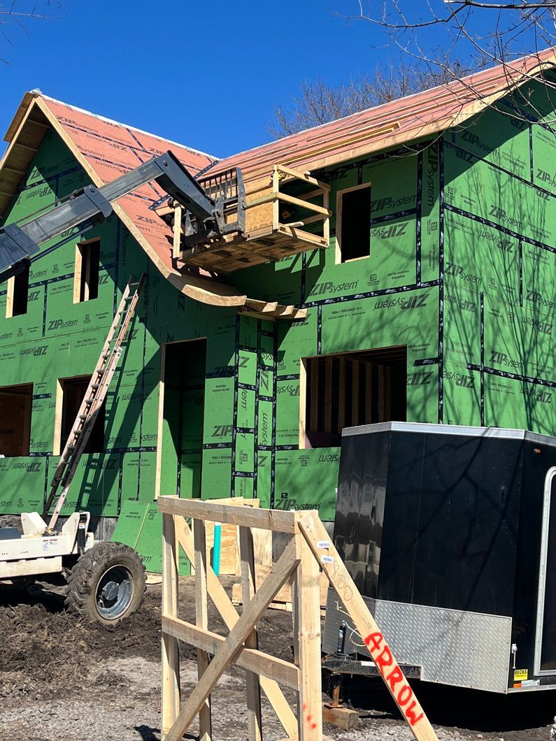 A house under construction, with green sheathing, lift, and wooden scaffolding.