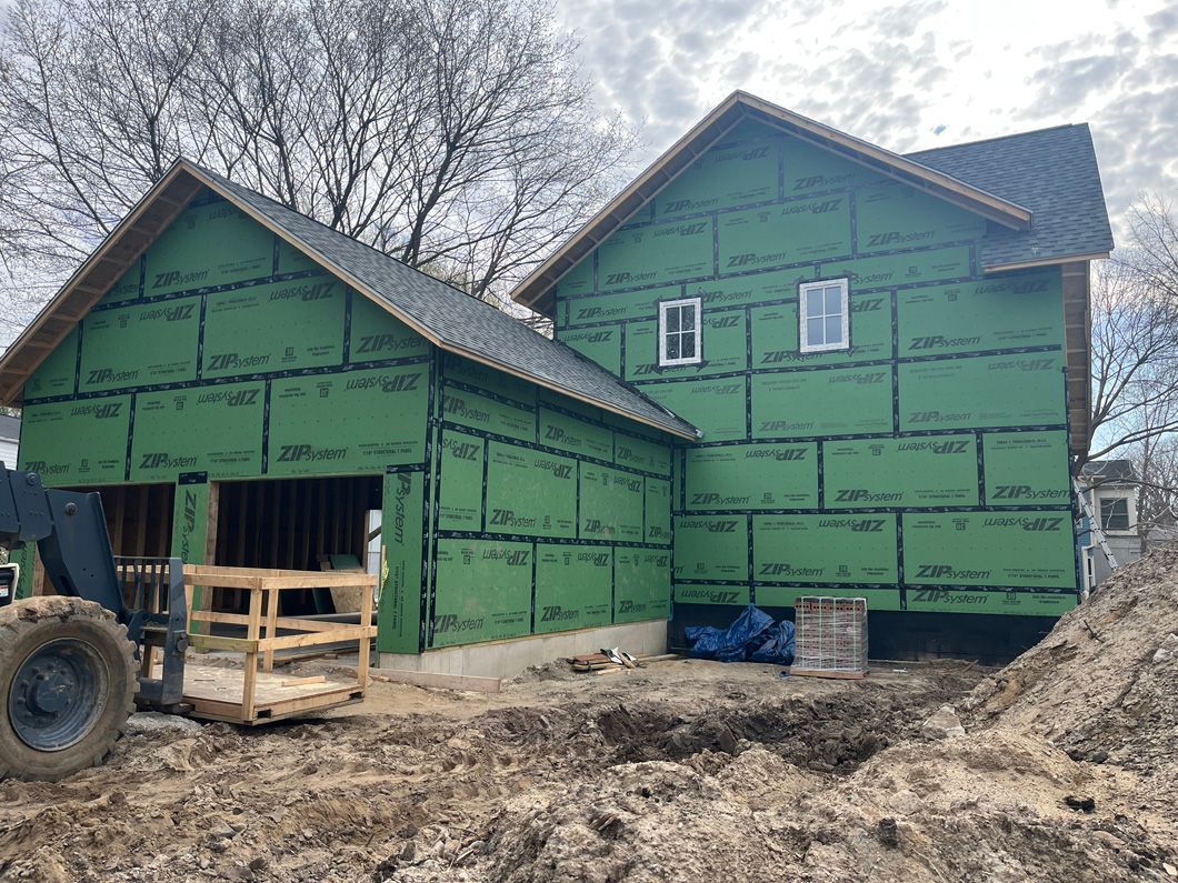 New house under construction, covered in green sheathing, with dirt and a front-end loader.