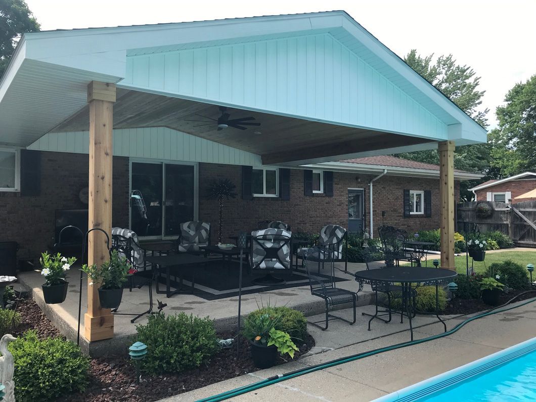 A covered patio with seating, by a pool next to a brick house.
