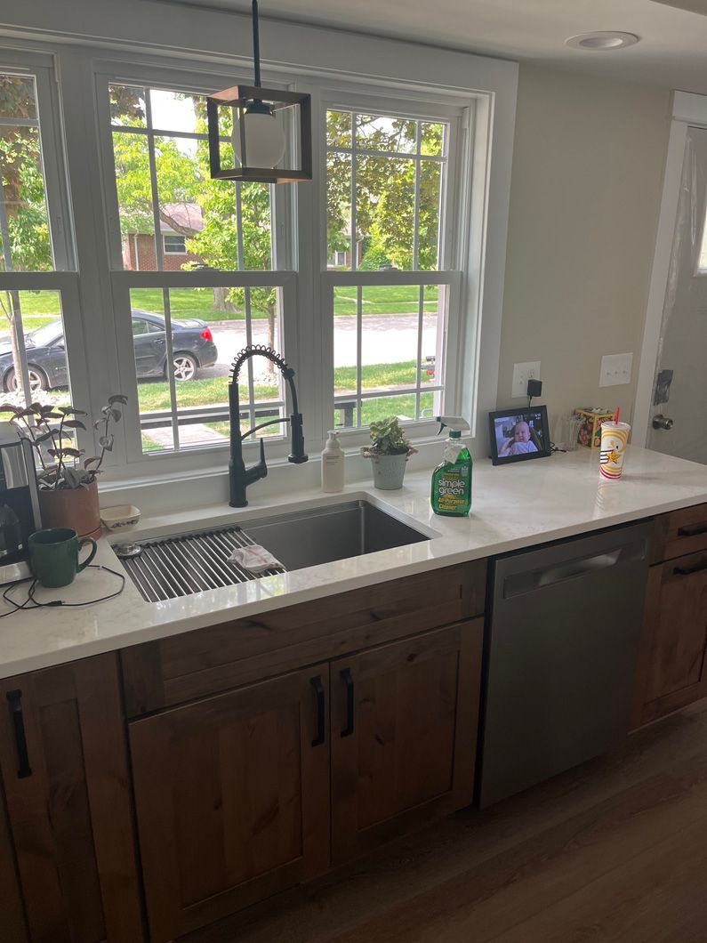 Kitchen with wood cabinets, white countertops, stainless steel sink, window, and black faucet.