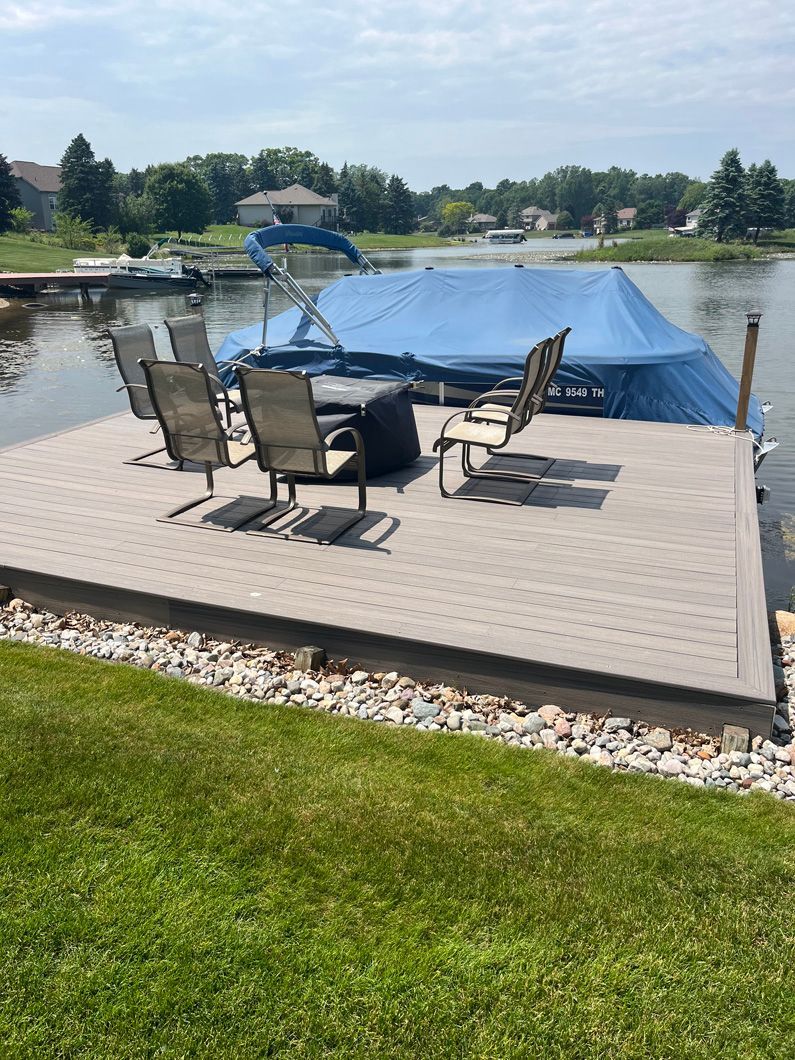 Dock on a lake with gray platform, chairs, boat cover, and green grass.