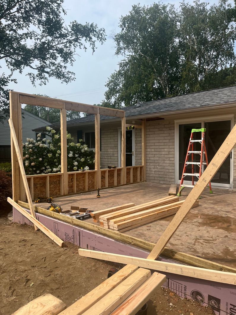 Construction of a wooden porch or sunroom on a residential property with a ladder and trees.