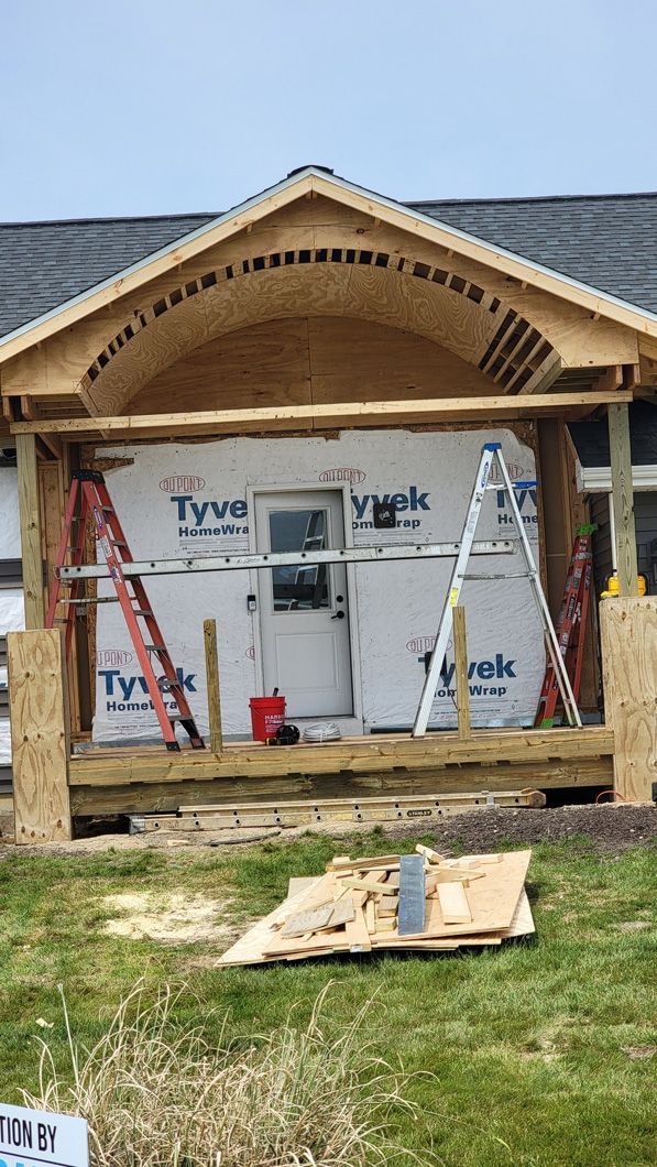 Construction of a porch with a curved roof. Ladders, wooden beams, and Tyvek wrap are visible.