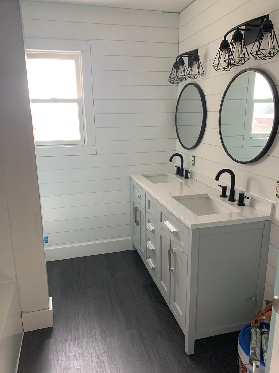 Bathroom with white shiplap walls, a double vanity, black mirrors, and dark gray flooring.