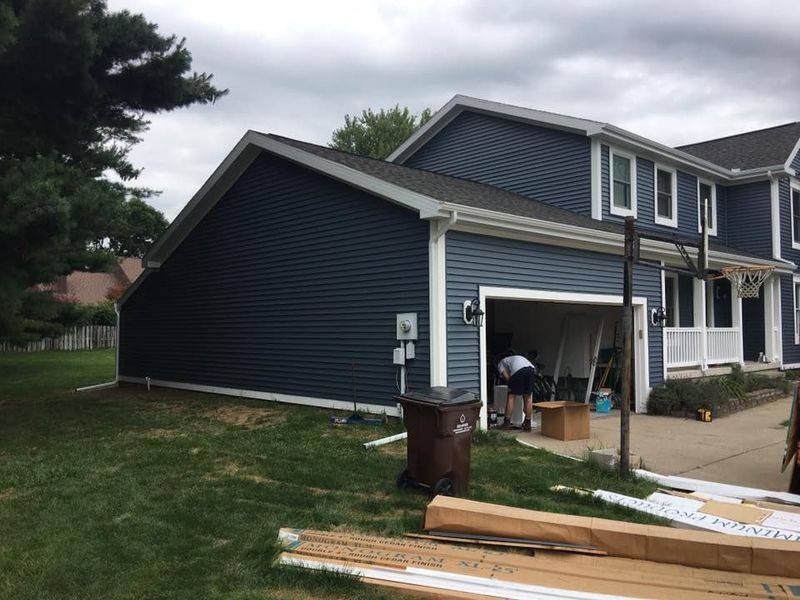Blue sided house with open garage and person inside, cloudy day.