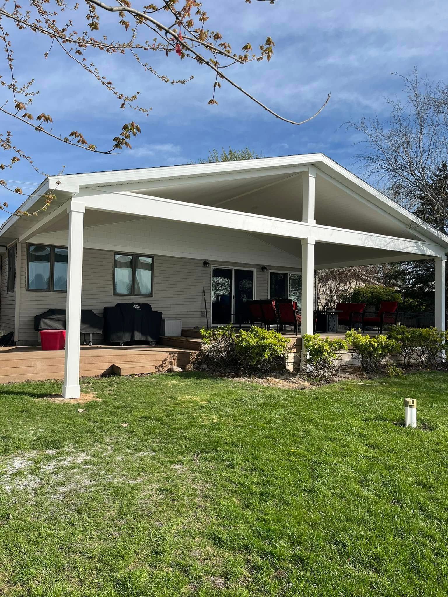 White patio cover over a light-colored house with windows and doors, backyard with grass, and blue sky.