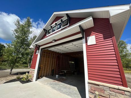 Red barn-style garage with open door; brown accents, white trim, and stone base. Bright blue sky.