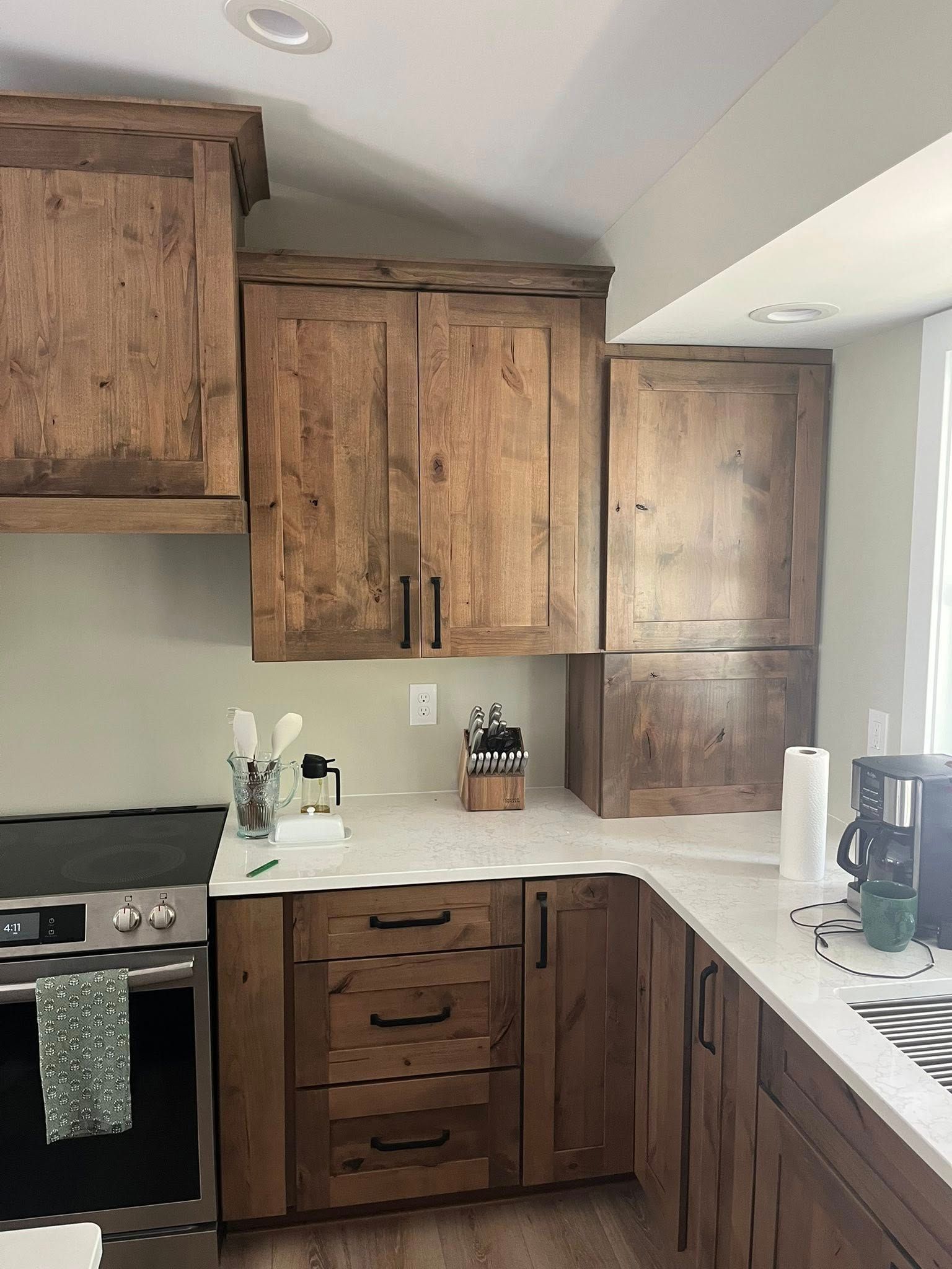 Rustic kitchen with wooden cabinets and white countertops; appliances and utensils visible.
