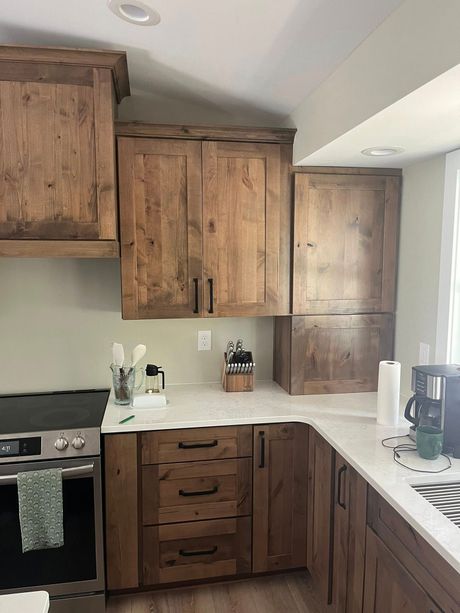 Rustic kitchen with wooden cabinets and white countertops; appliances and utensils visible.