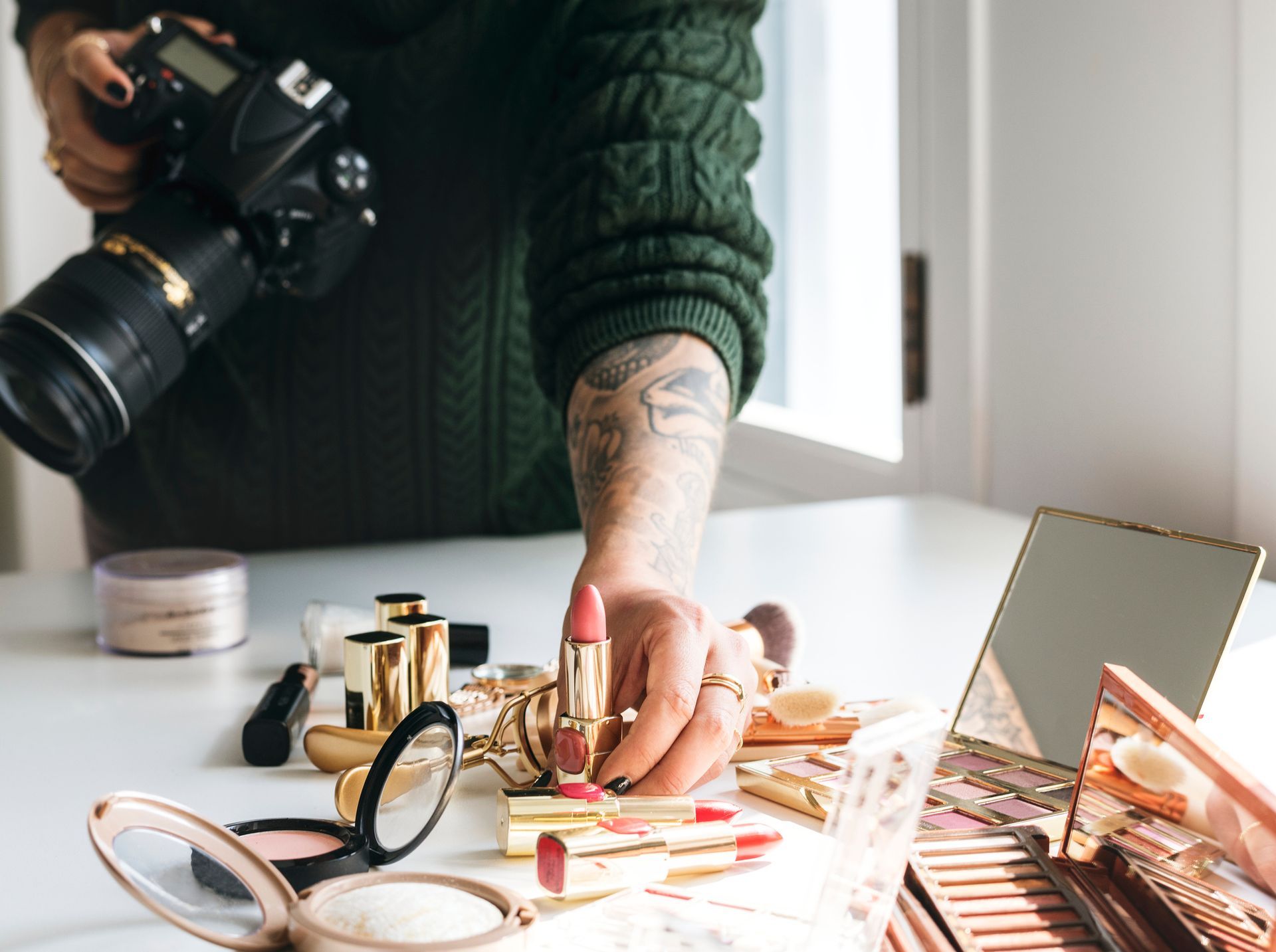 Person holding camera, arranging makeup products on a white surface, indoors.