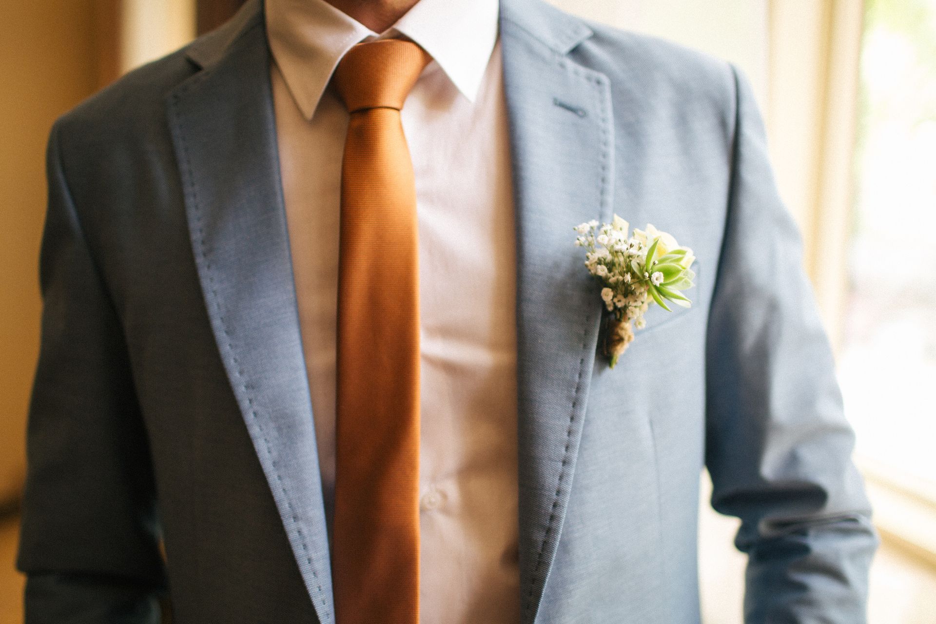 Man in blue suit with an orange tie and a boutonniere.