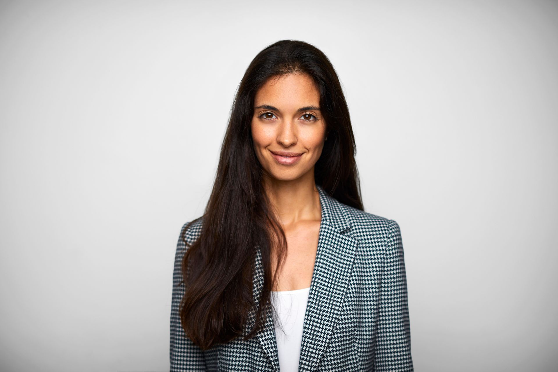 Woman in a blue and white checkered blazer smiles at the camera against a white backdrop.