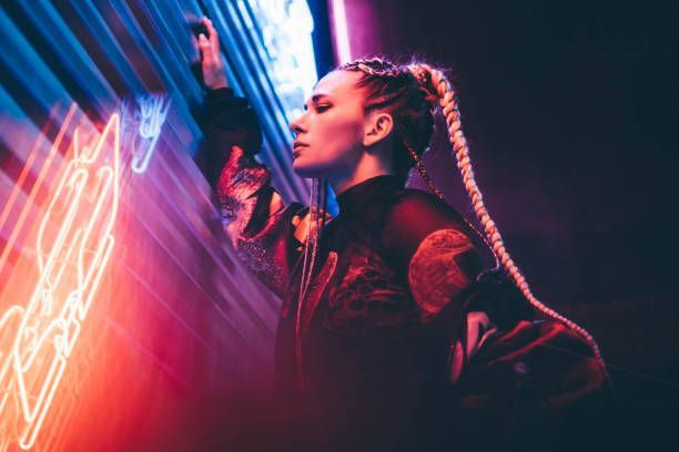 Woman with braid, leaning against wall, lit with neon lights.