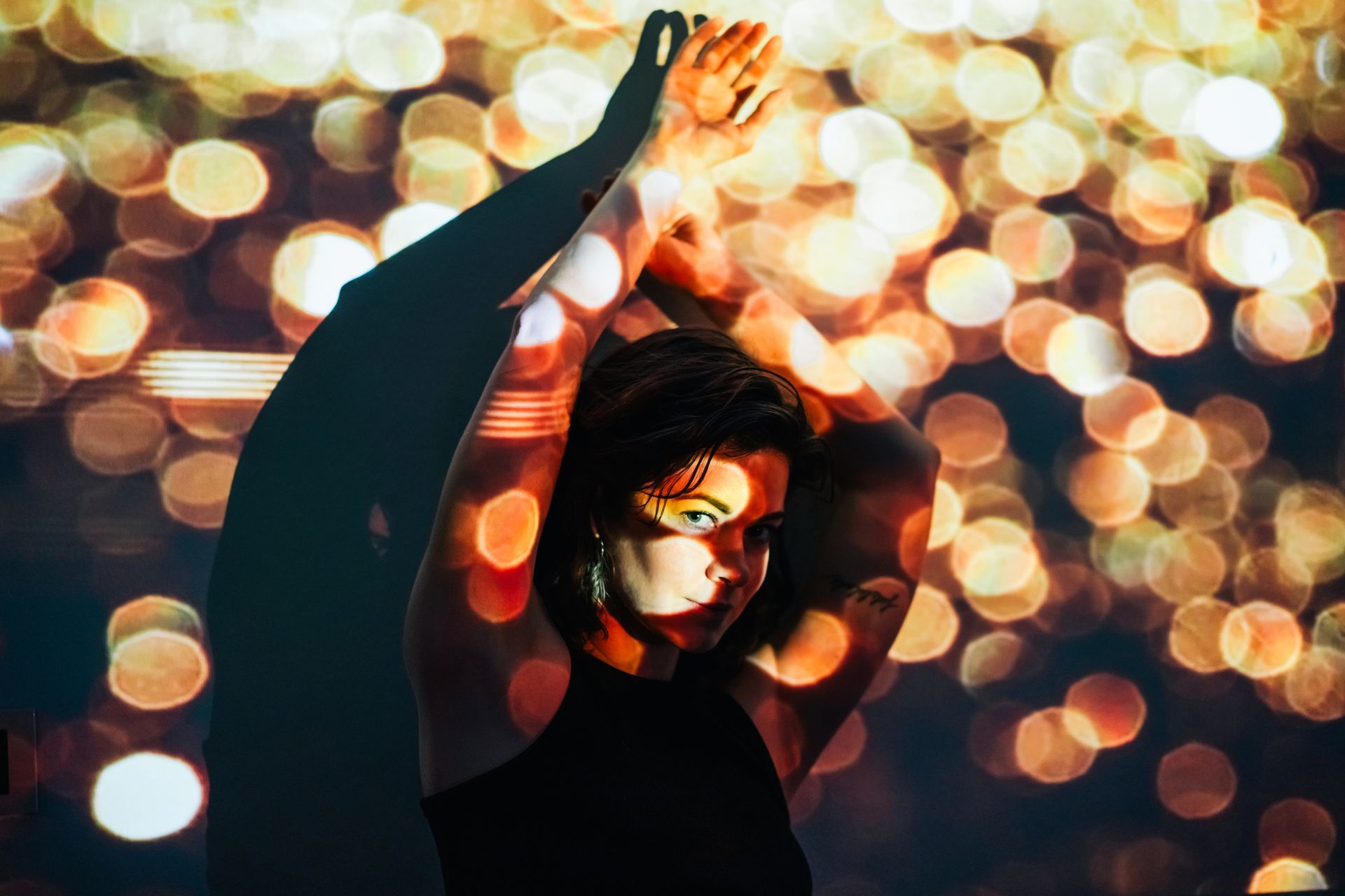 Woman with arms raised, illuminated by bokeh lights and shadow.