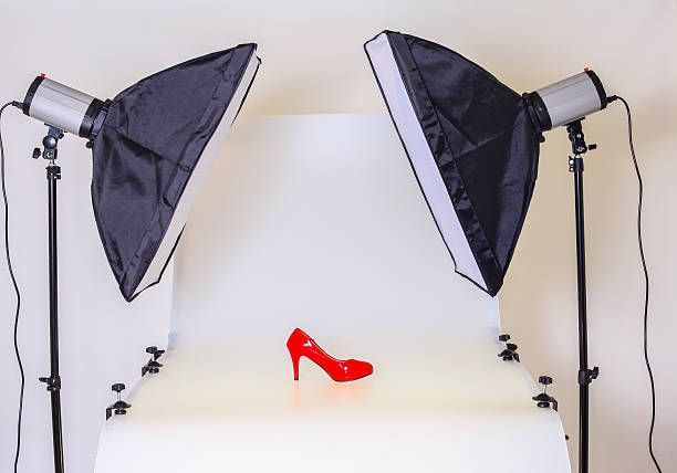 Red high heel shoe on white surface, illuminated by two studio lights.