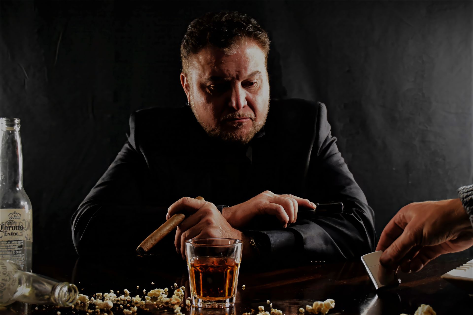 Man in suit, holding cigar, looking intently at cards; table with drink, bottle, popcorn.