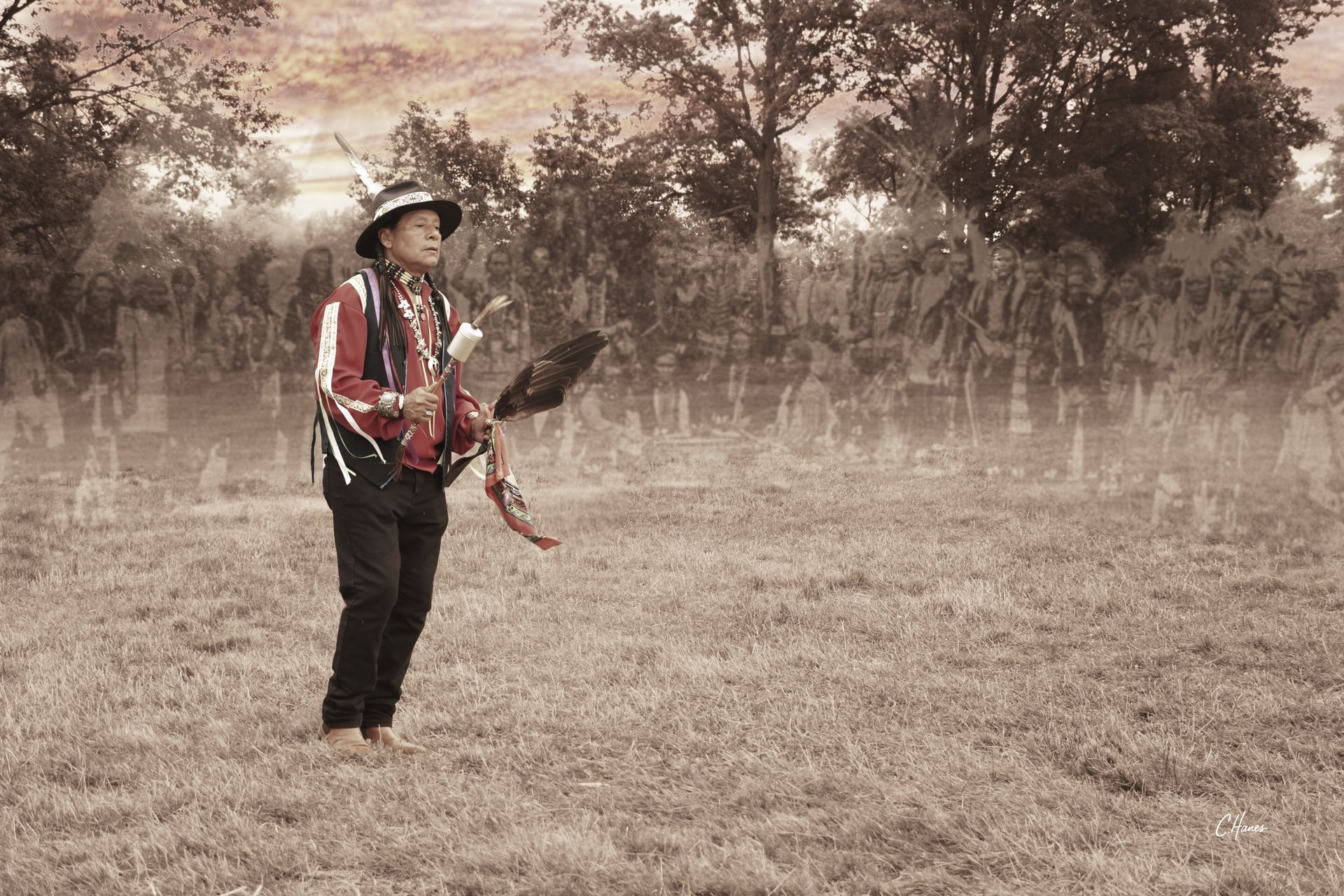 Person in traditional clothing stands holding an object in a grassy field. Sepia tone.