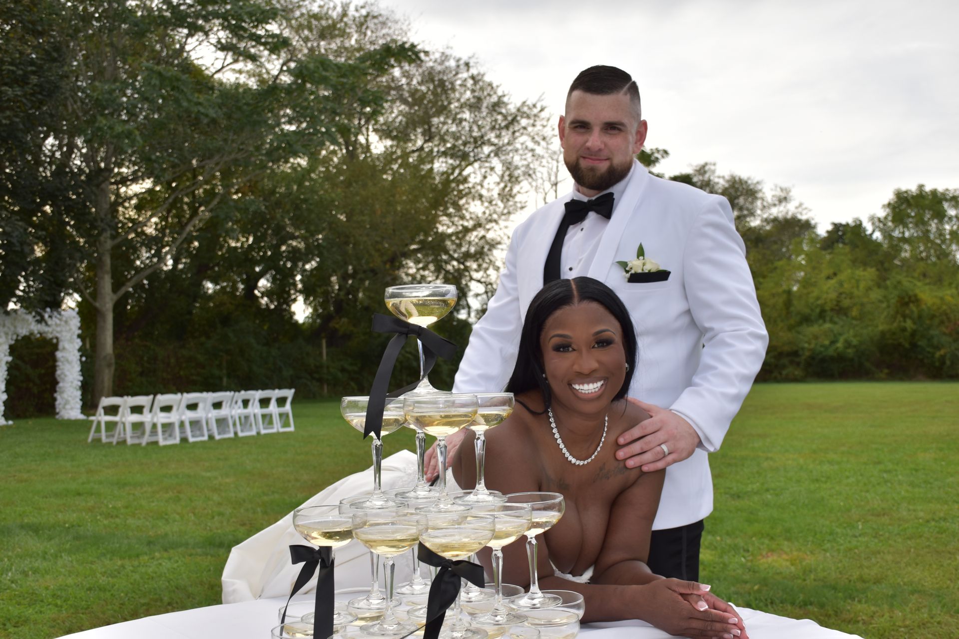 Couple poses with champagne tower at outdoor wedding.