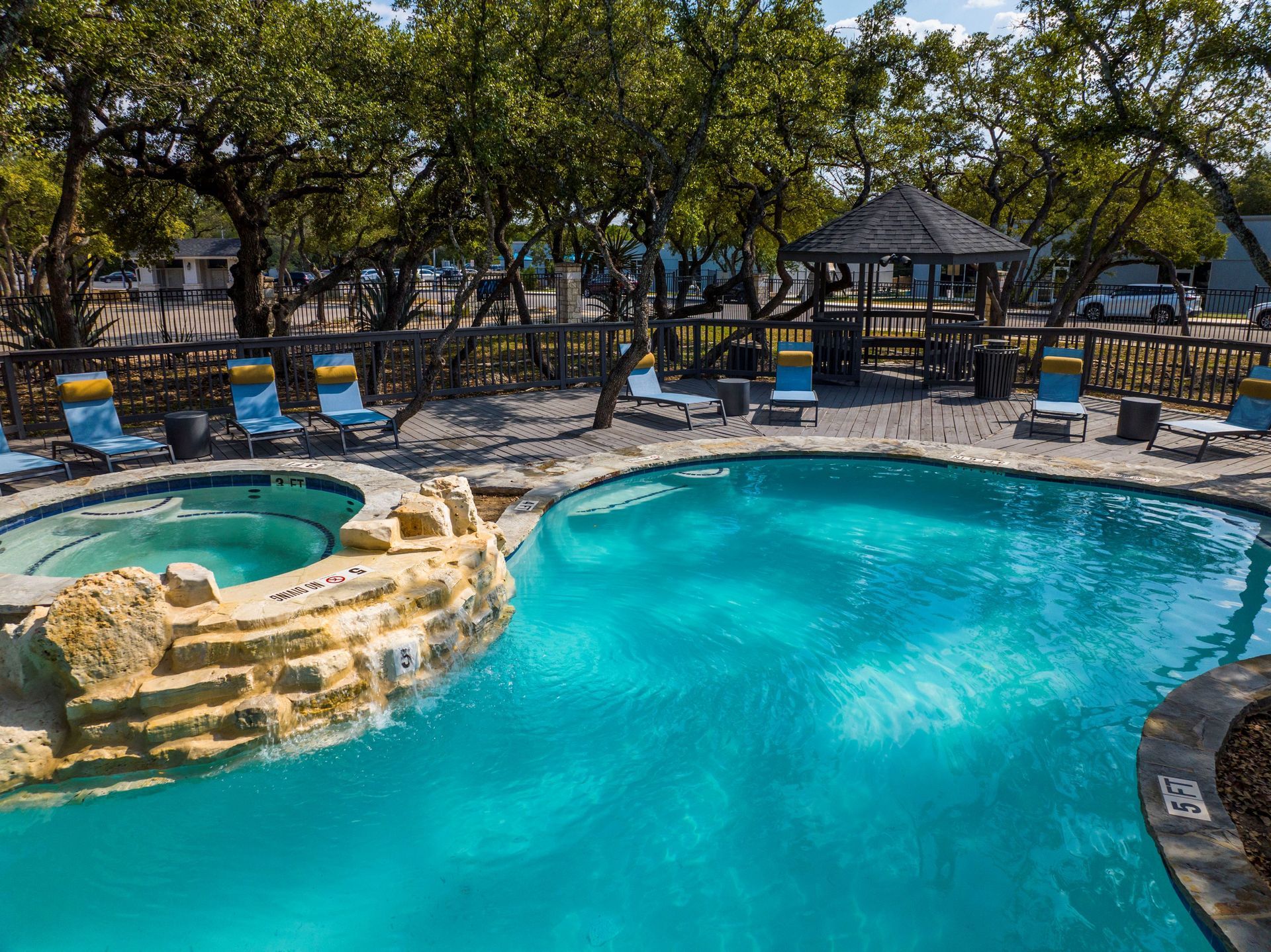 A large swimming pool with a hot tub in the middle surrounded by chairs and trees at Allure at Shavano.
