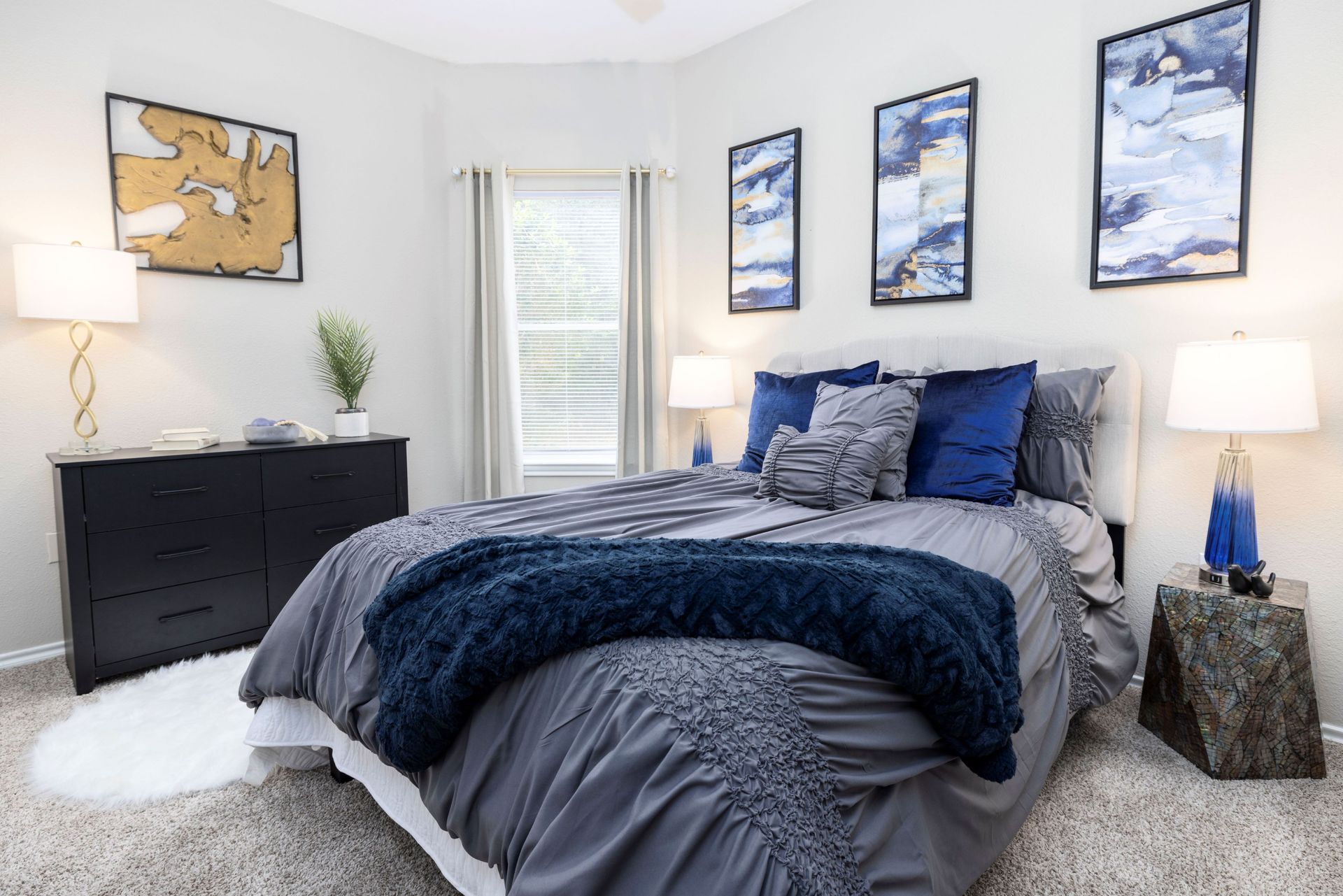 A bedroom with a bed , dresser , lamps and paintings on the wall at Allure at Shavano.