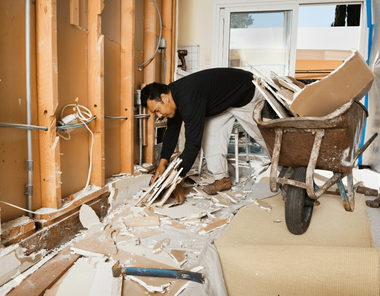 A person inside a gutted room gathers debris, placing it into a wheelbarrow.