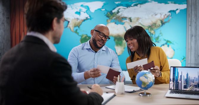 Travel agency consultant reviewing trip plans with two clients holding passports.
