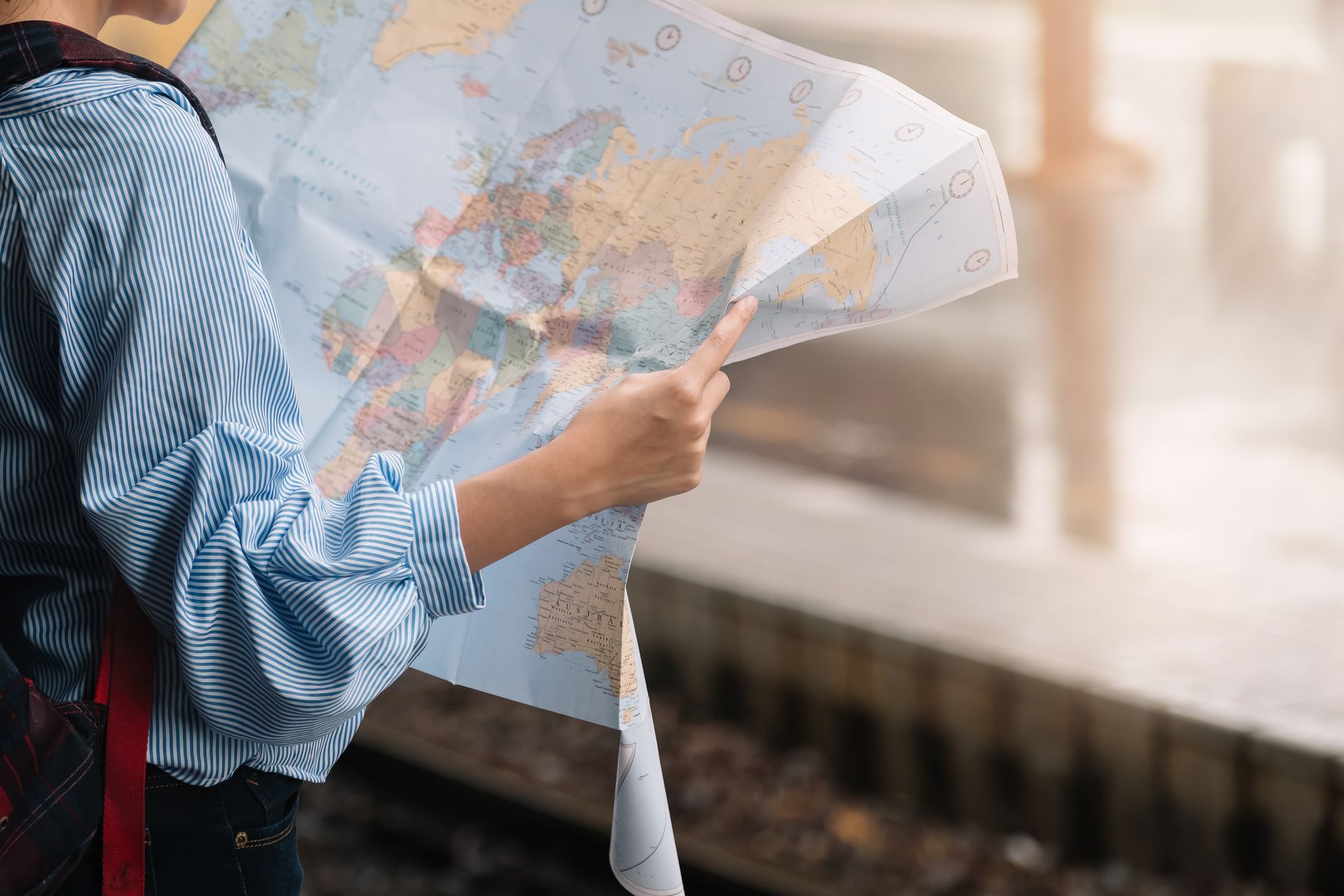 Traveler holding an unfolded world map while standing near a train platform.