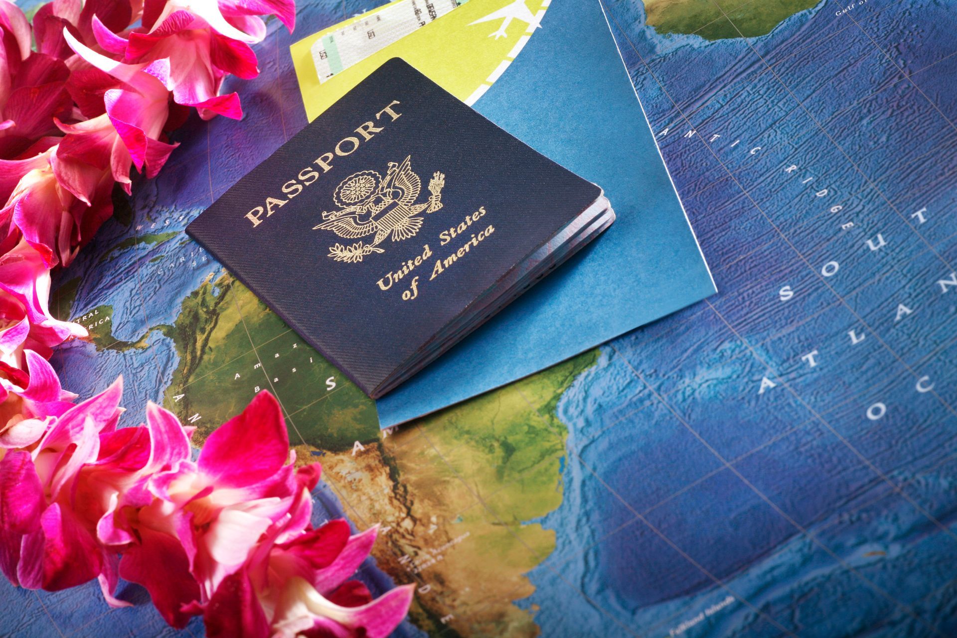 A U.S. passport and boarding pass placed on a world map with pink Hawaiian leis.