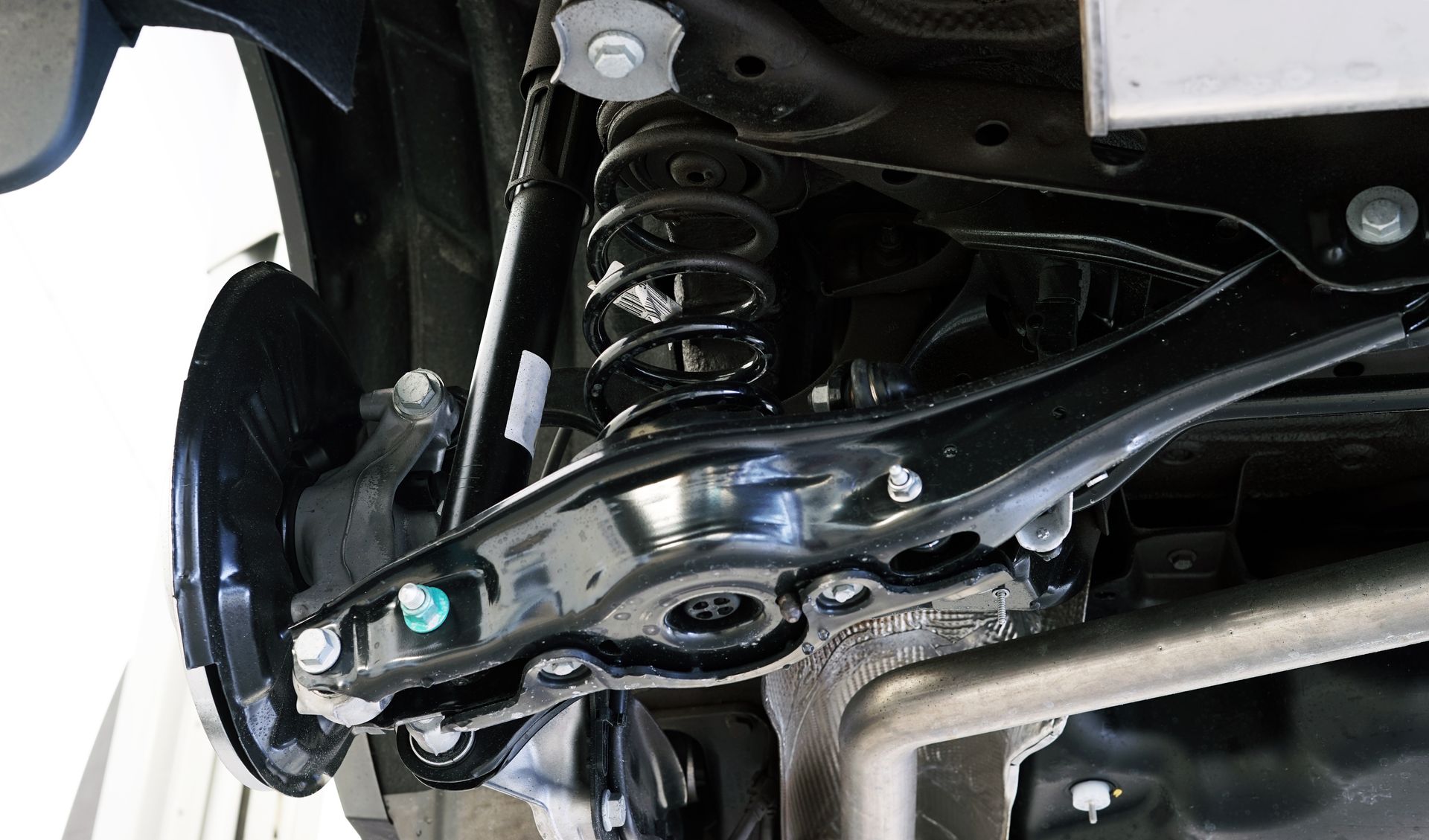 Undercarriage of a black vehicle, showing suspension components: spring, arm, brake rotor, exhaust pipe. | Integrity Performance Automotive