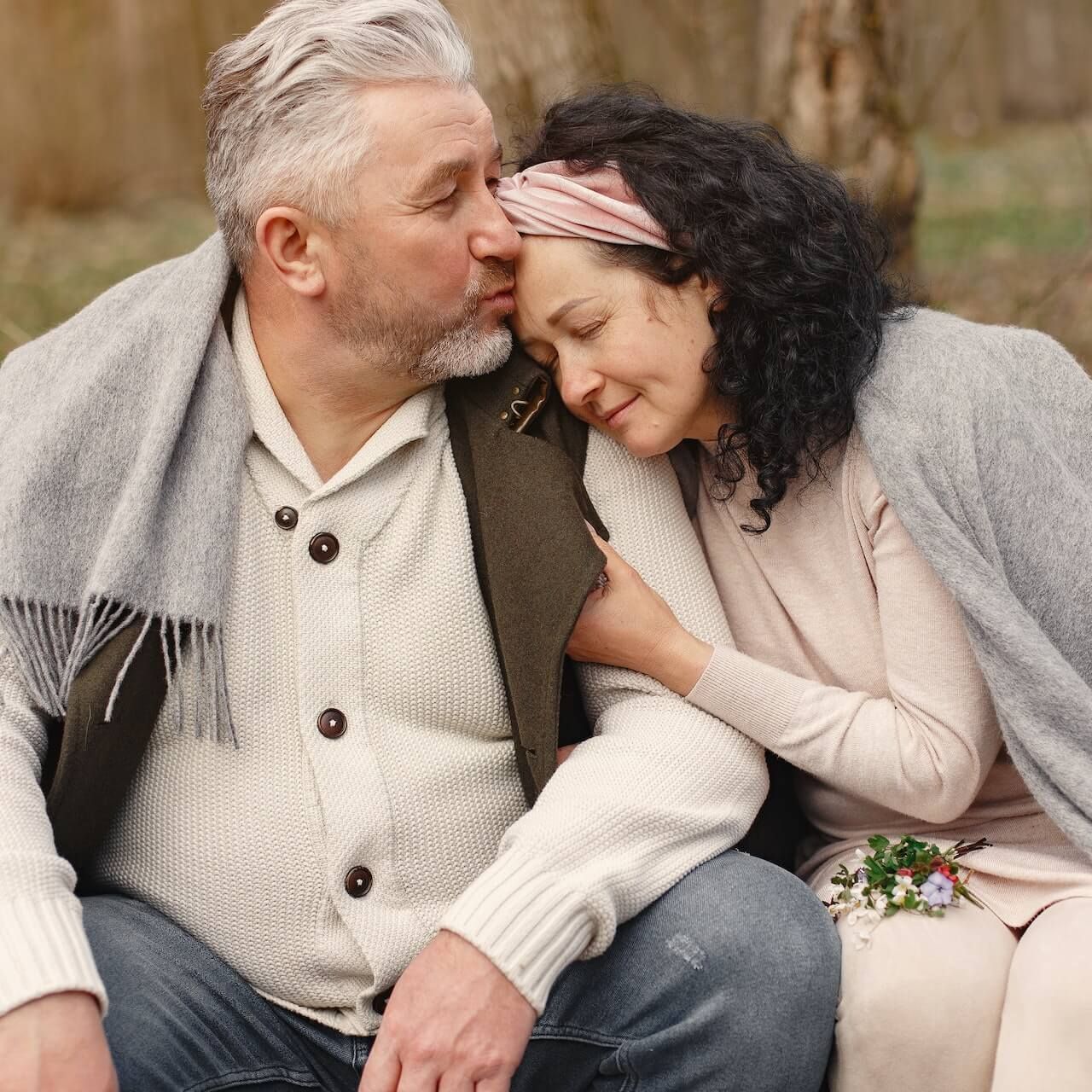 A man is kissing a woman on the forehead while sitting on a bench.