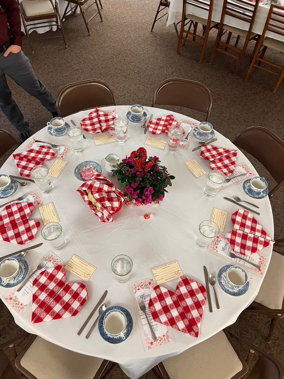 A round table with red and white checkered napkins and utensils on it