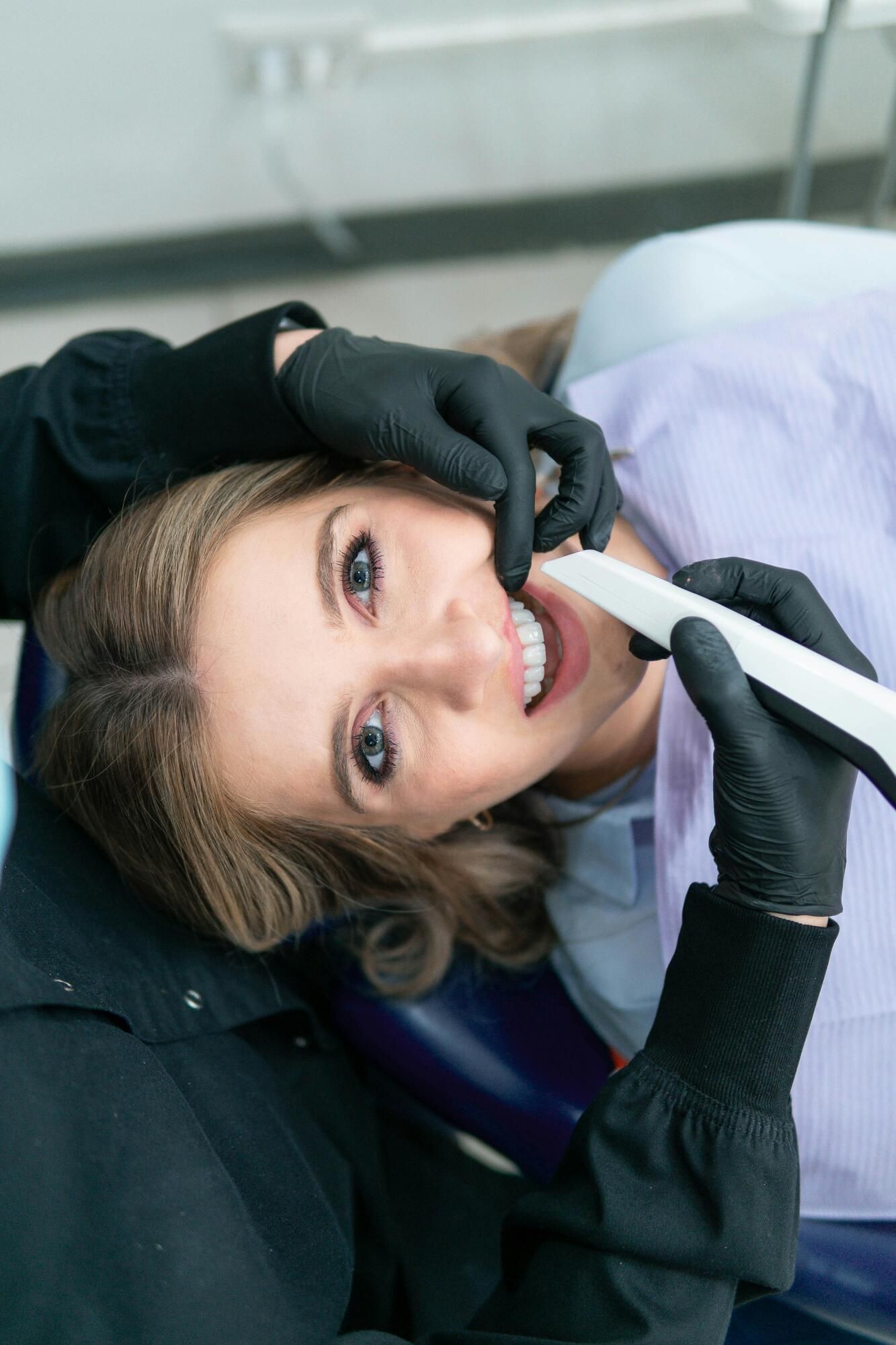 A dental professional in black gloves uses an intraoral scanner on a patient, who is lying back in a dental chair.