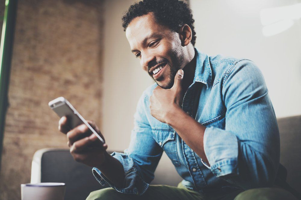 A man is sitting on a couch looking at his cell phone.