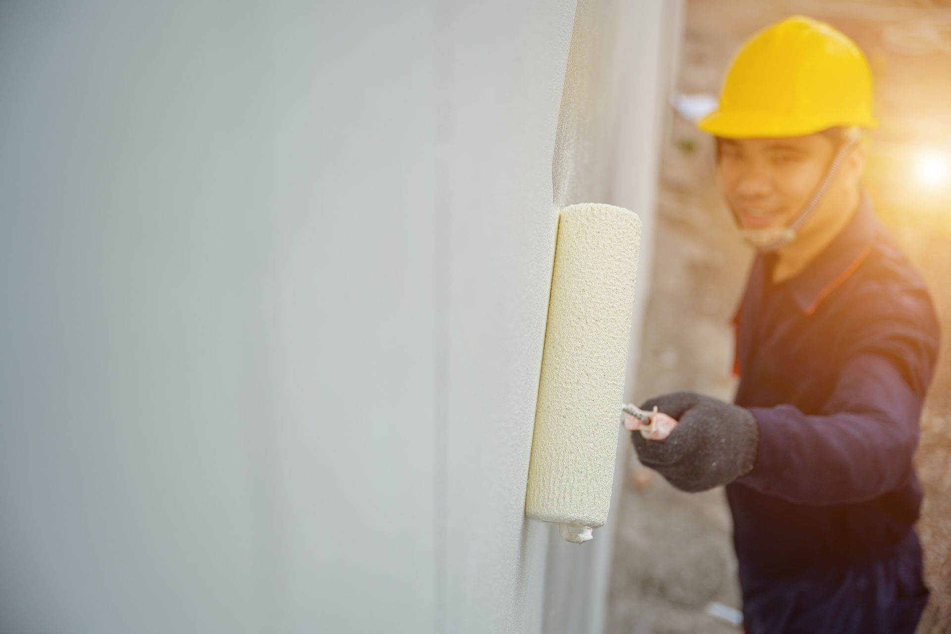 A painter expertly paints a house while gripping a paint roller.