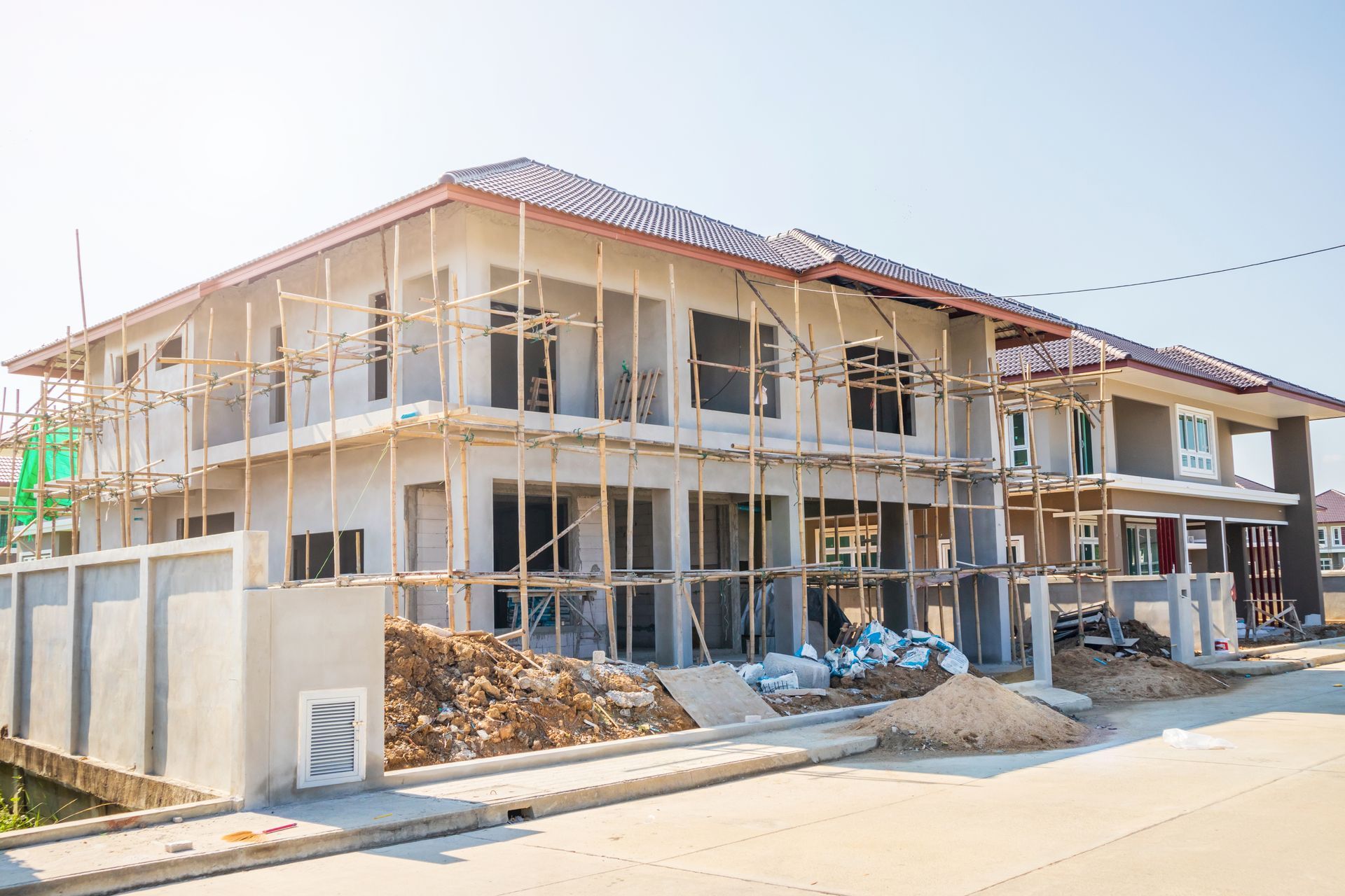 Two-story house under construction with scaffolding and building materials on a sunny day.
