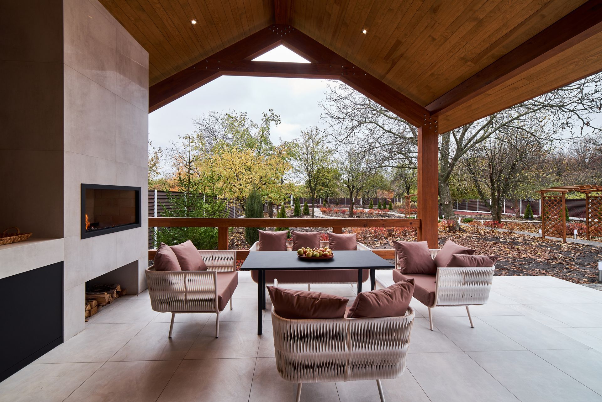 Covered patio with seating, fireplace, and a view of a yard with trees.