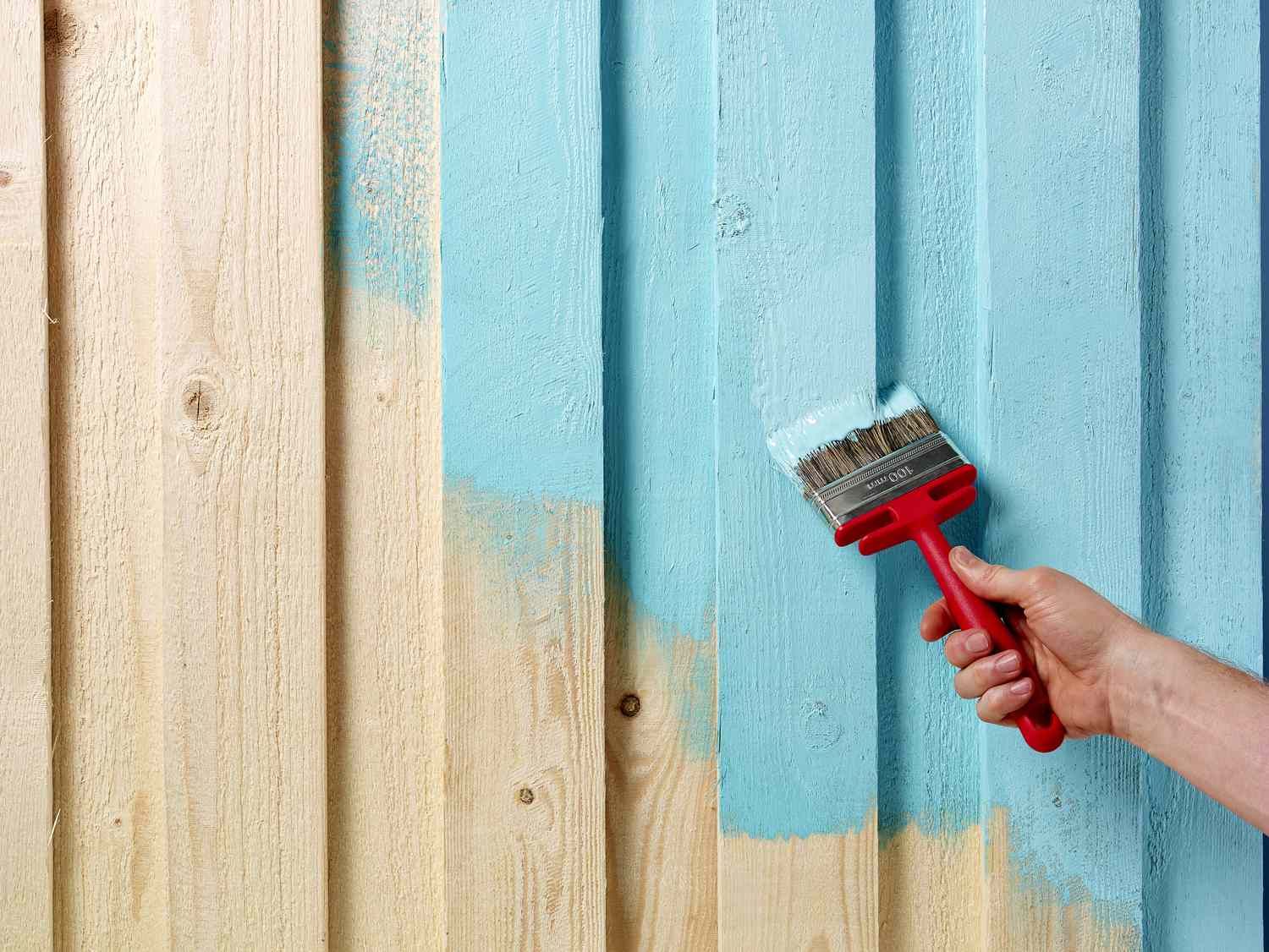 An image of a wooden fence being painted blue, with smooth strokes and vibrant color transforming its appearance.