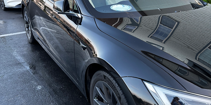 Black sedan parked on a wet street, viewed from the front side.