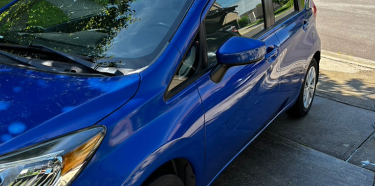 Blue compact car parked on a driveway beside a curb and street