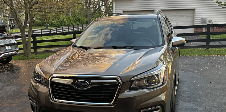 Brown SUV parked in a driveway, front view, with a house and black fence in the background