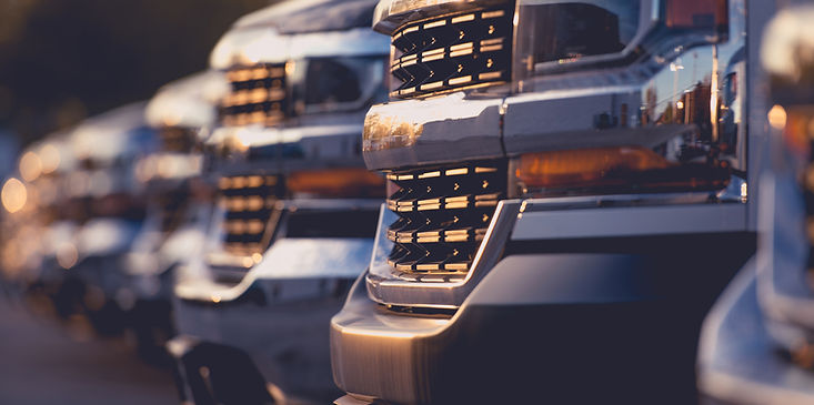 Parked pickup trucks lined up in a snowy lot at dusk, headlights glowing warm against the cold scene