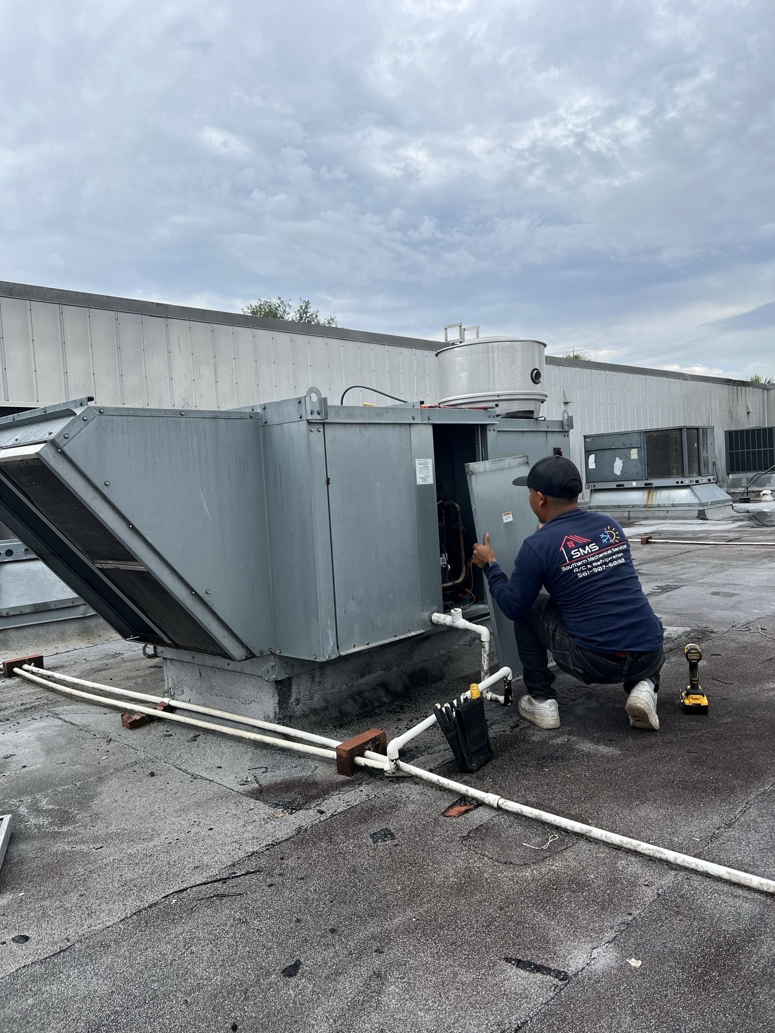 A man is working on an air conditioner on the roof of a building.