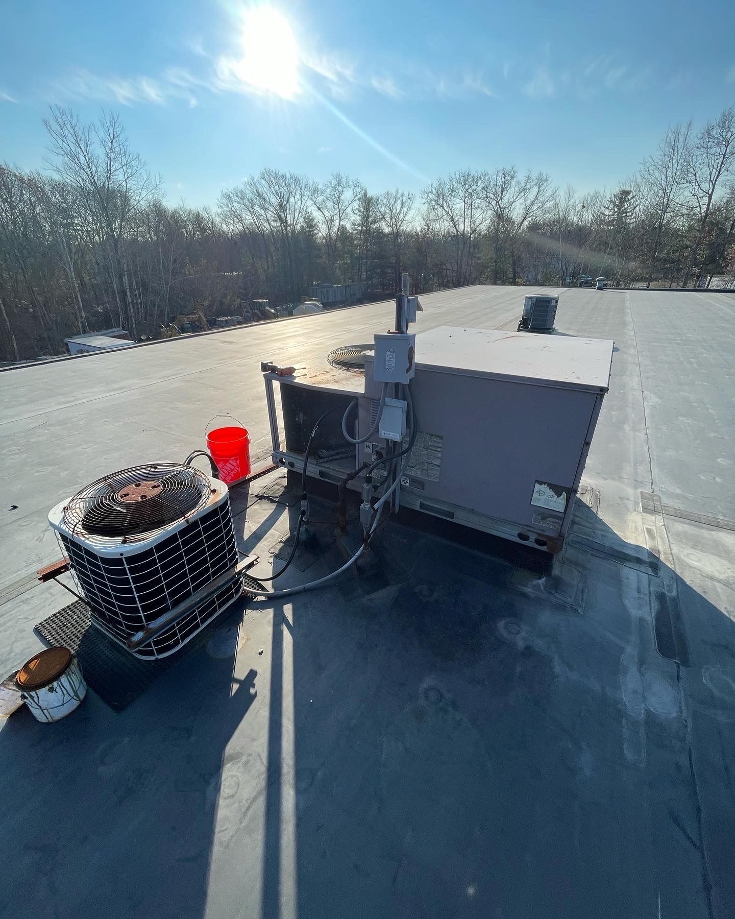 HVAC unit on a flat roof under a bright sky.  A red bucket and open paint can sit nearby.